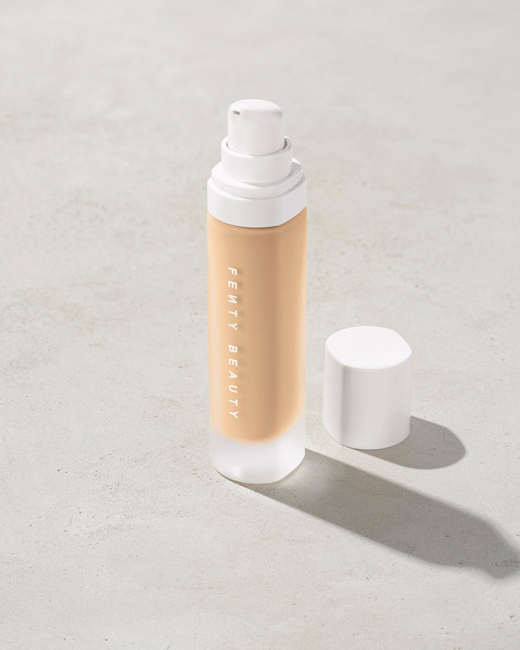 open bottle of Fenty Beauty Pro Filt'r Soft Matte Longwear Foundation with pump dispenser in shade #185 on concrete background