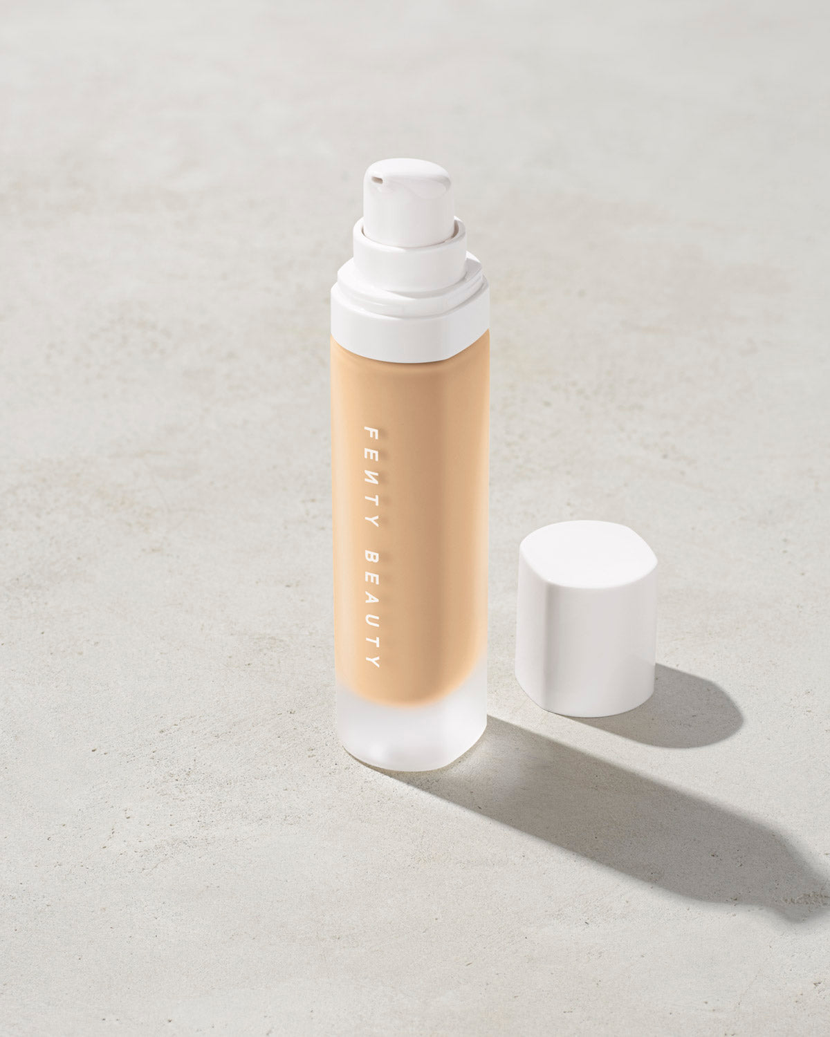 open bottle of Fenty Beauty Pro Filt'r Soft Matte Longwear Foundation with pump dispenser in shade #185 on concrete background