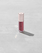 A closed tube of Gloss Bomb Universal Lip Luminizer in the shade RiRi on a grey background.